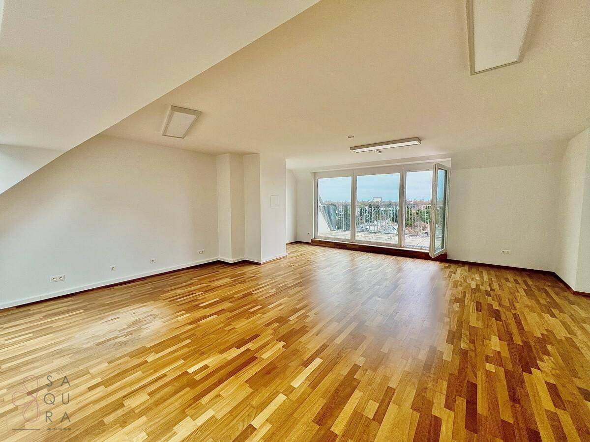 Geräumiger, heller Wohnraum mit Holzboden und großen Fenstern, die einen weiten Blick über die Stadt bieten.