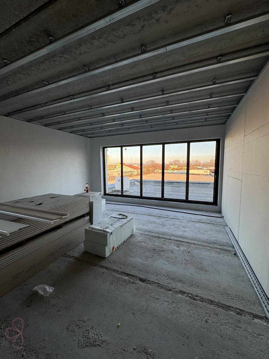 Baustelle eines Büroraums mit großen Fenstern, die viel Licht hereinlassen, und gestapelten Baumaterialien.
