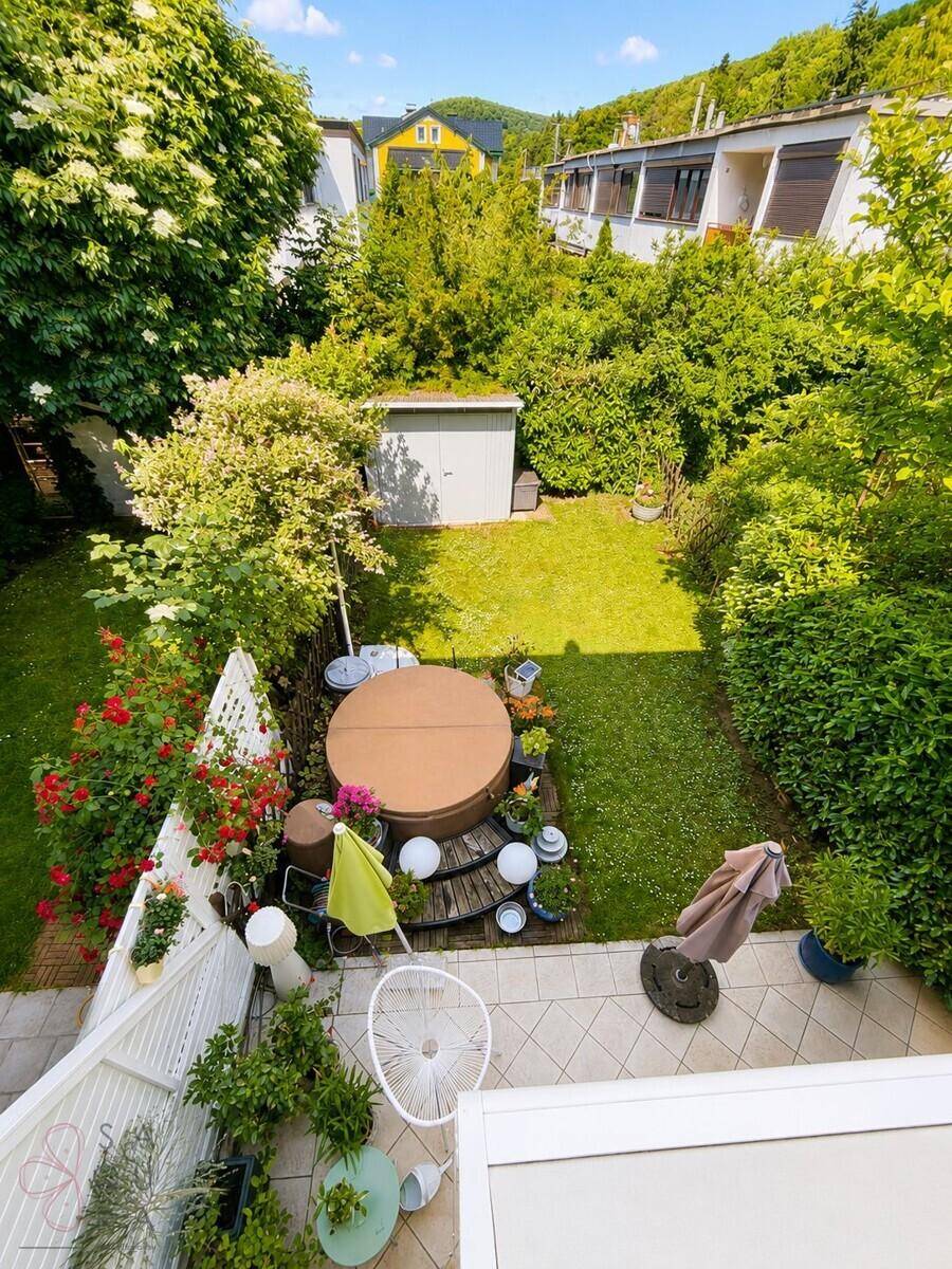 Gepflegter Garten mit Whirlpool, Rasenfläche, Gartenhaus und üppiger Bepflanzung.