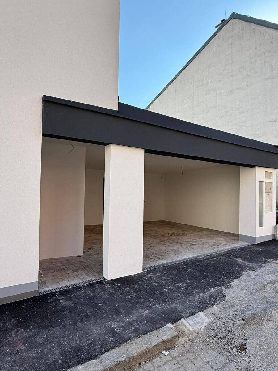 Offener Carport-Bereich mit Säulen und Zugangstüren, ideal für zwei Fahrzeuge.