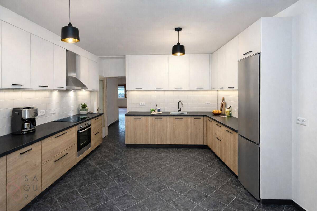 Moderne Küche mit weißen und holzfarbenen Schränken, dunkler Arbeitsplatte und Fliesenboden.