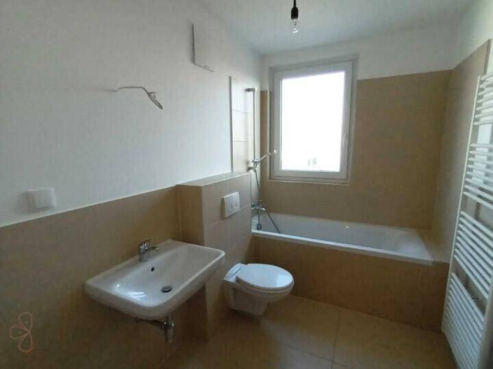 Helles Badezimmer mit Badewanne, WC, Waschbecken und einem Fenster für Tageslicht.