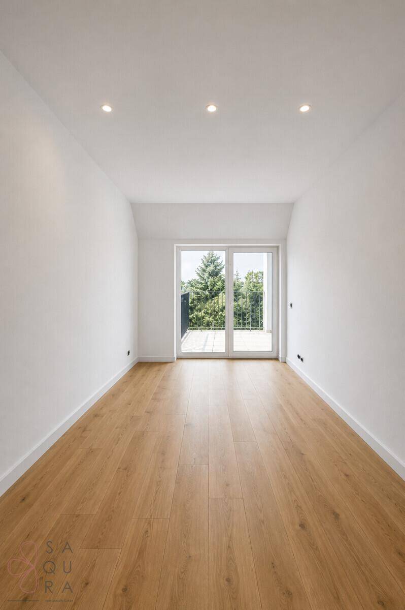 Helles, leeres Schlafzimmer mit Holzboden und großem Fenster mit Zugang zum Balkon.