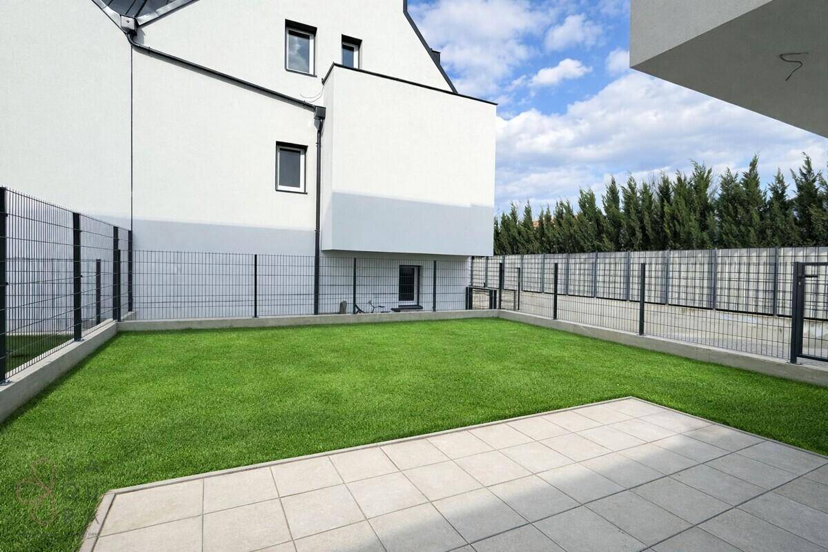 Gepflegter Gartenbereich mit Rasenfläche und gepflasterter Terrasse hinter dem Gebäude.
