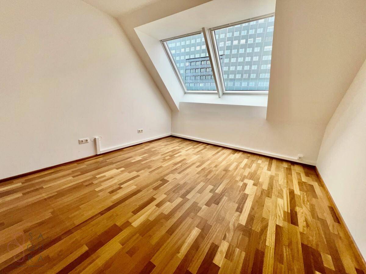 Helles Schlafzimmer mit Holzboden, Dachschrägen und einem großen Dachfenster, das den Raum mit Licht füllt.