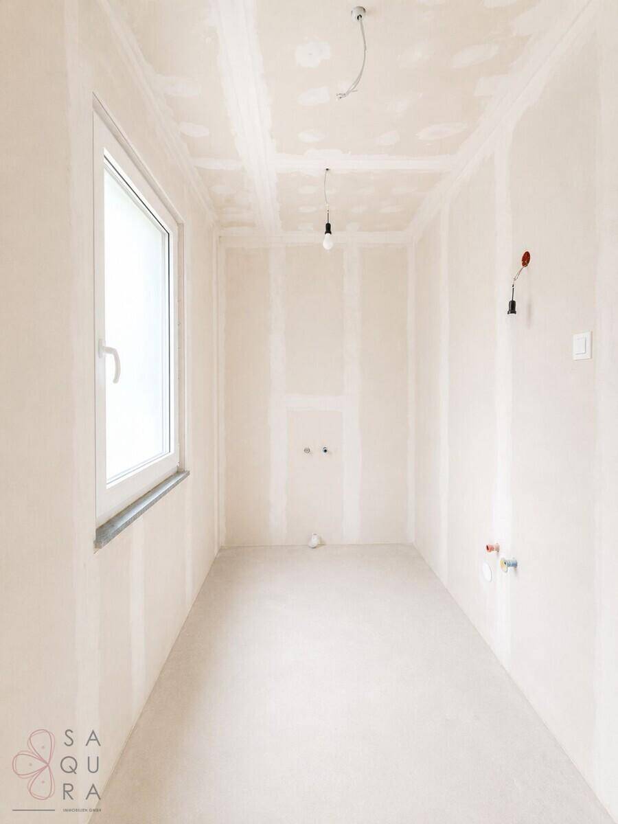 Unfertiges Badezimmer im Rohbau mit Fenster und Anschlüssen für Sanitäranlagen.