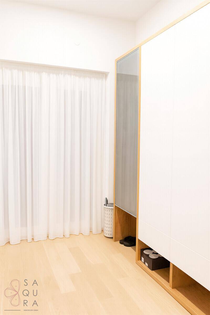 Heller Raum mit großem Fenster und Vorhängen, Parkettboden und modernem Kleiderschrank.