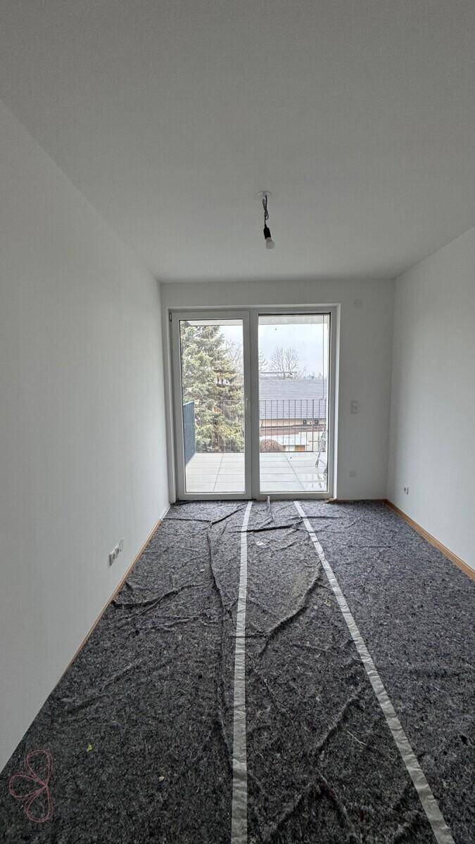Raum im Bauzustand mit Balkonzugang und vorbereitetem Unterboden, bereit für den weiteren Ausbau.
