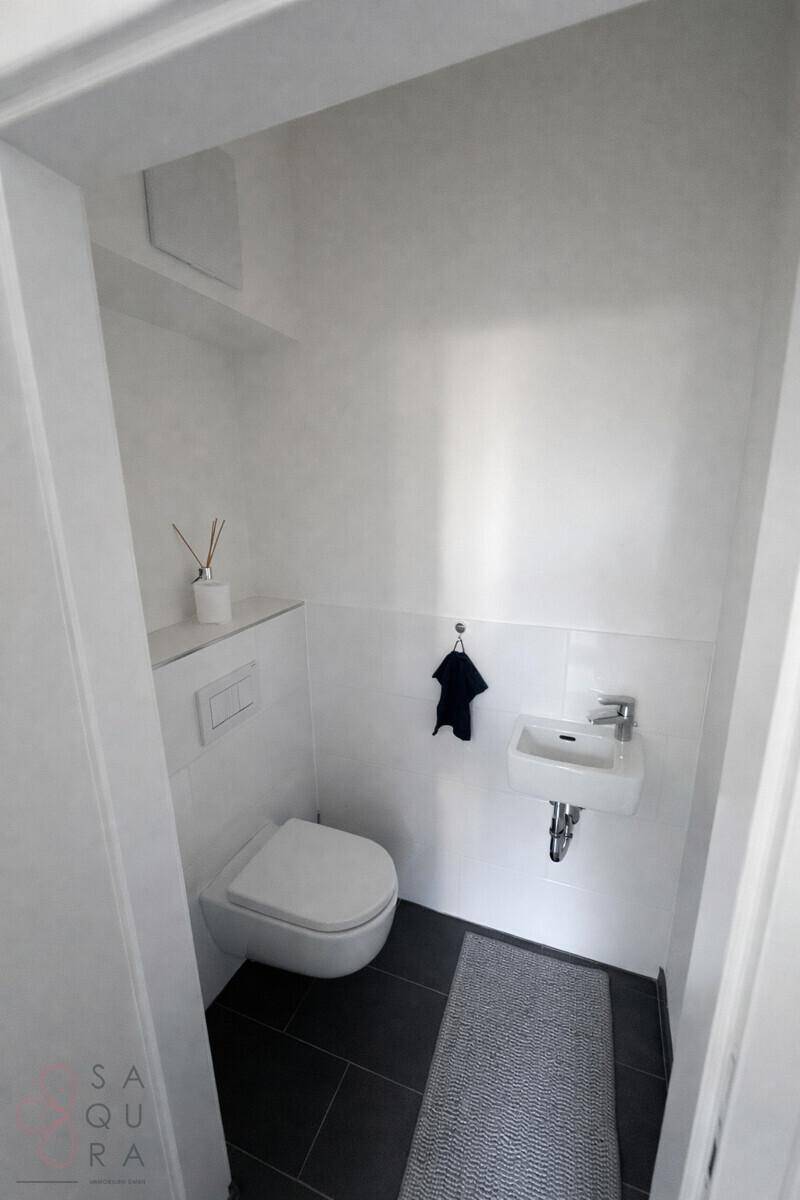 Kleines Gäste-WC mit Wand-WC, Handwaschbecken und dunklen Bodenfliesen.