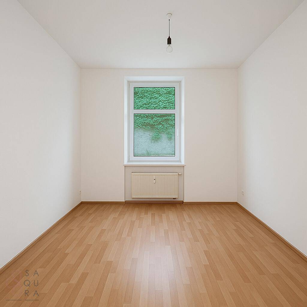 Leerer Raum mit Laminatboden und Fenster mit Blick auf grüne Vegetation.