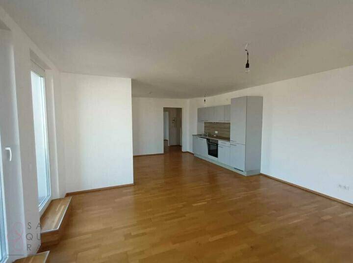 Geräumiger, leerer Wohn-Essbereich mit integrierter Küchenzeile und hellem Parkettboden.