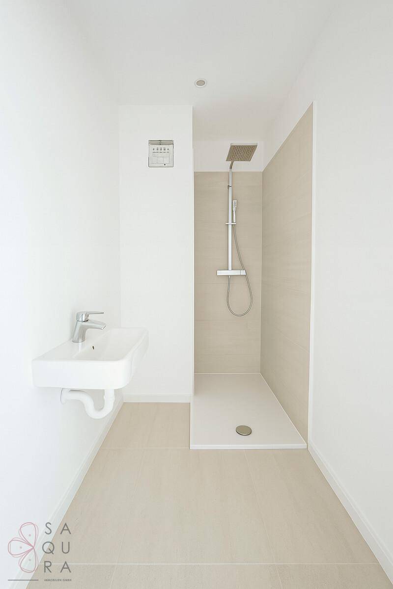 Modernes Badezimmer mit Einzelwaschbecken und begehbarer Dusche, in hellen Tönen gehalten.