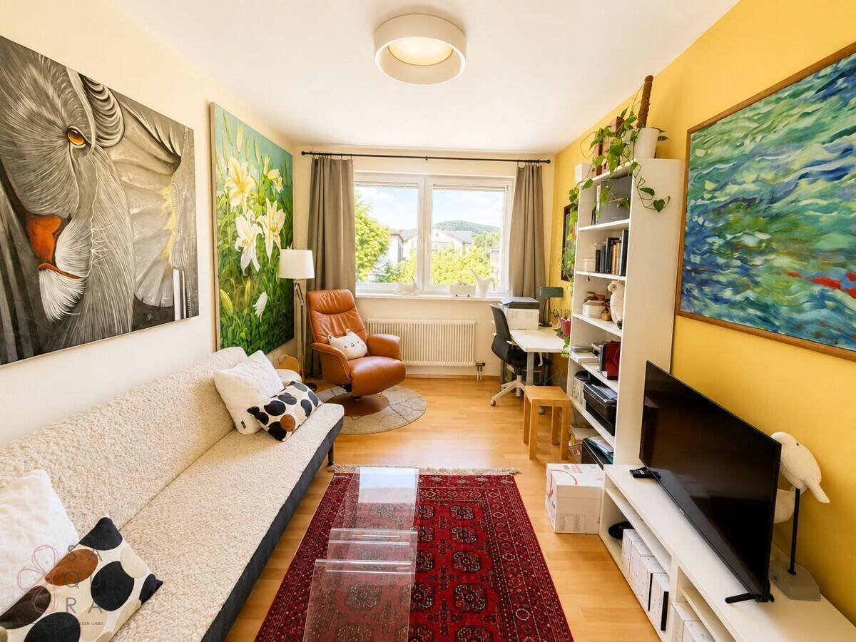 Helles Wohnzimmer mit Sofa, Schreibtisch und farbenfroher Dekoration.