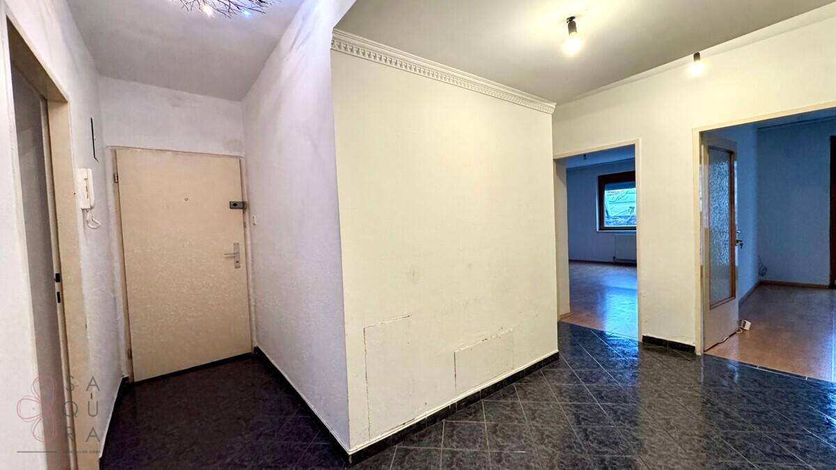 Leerer Eingangsbereich mit dunklem Fliesenboden und einer schlichten Eingangstür.