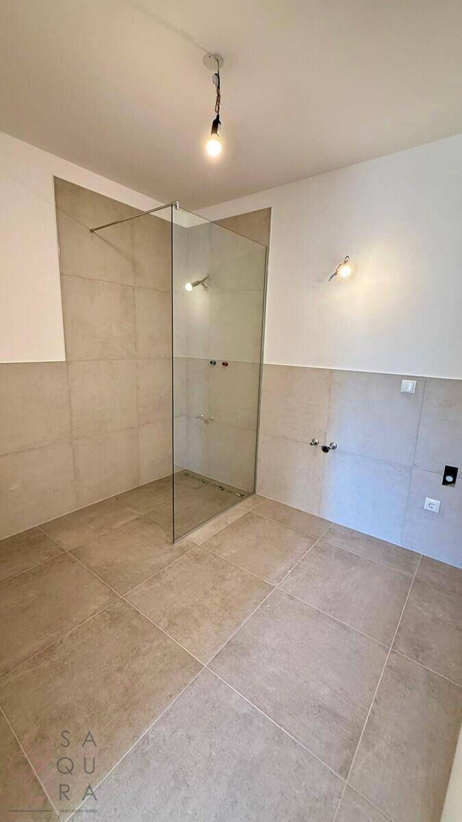 Unfertiges Badezimmer mit begehbarer Dusche und grauen Fliesen, bereit für die Installation der Armaturen.