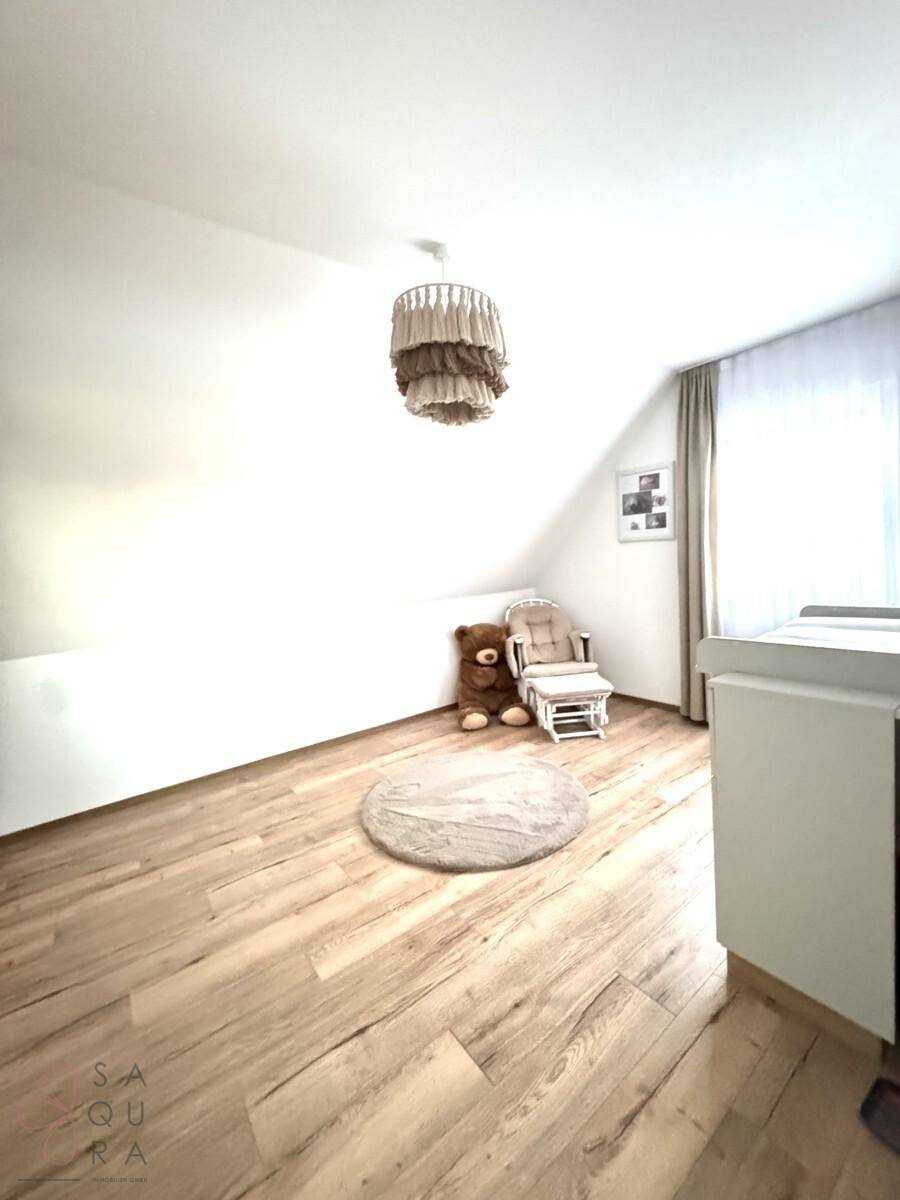 Kinderzimmer im Dachgeschoss mit Holzboden, Schaukelstuhl und viel Tageslicht.