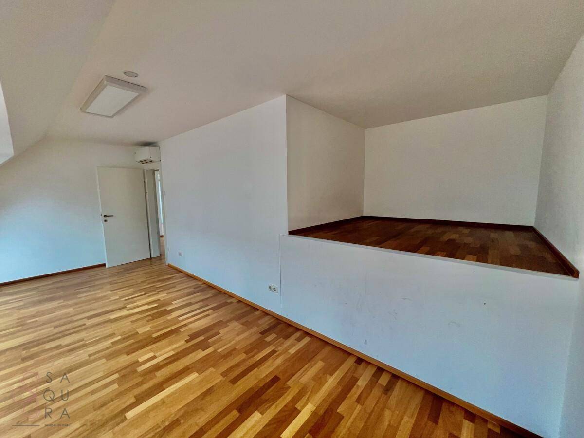 Helles Schlafzimmer mit Holzboden und einer erhöhten Fläche, ideal für einen begehbaren Kleiderschrank oder Stauraum.