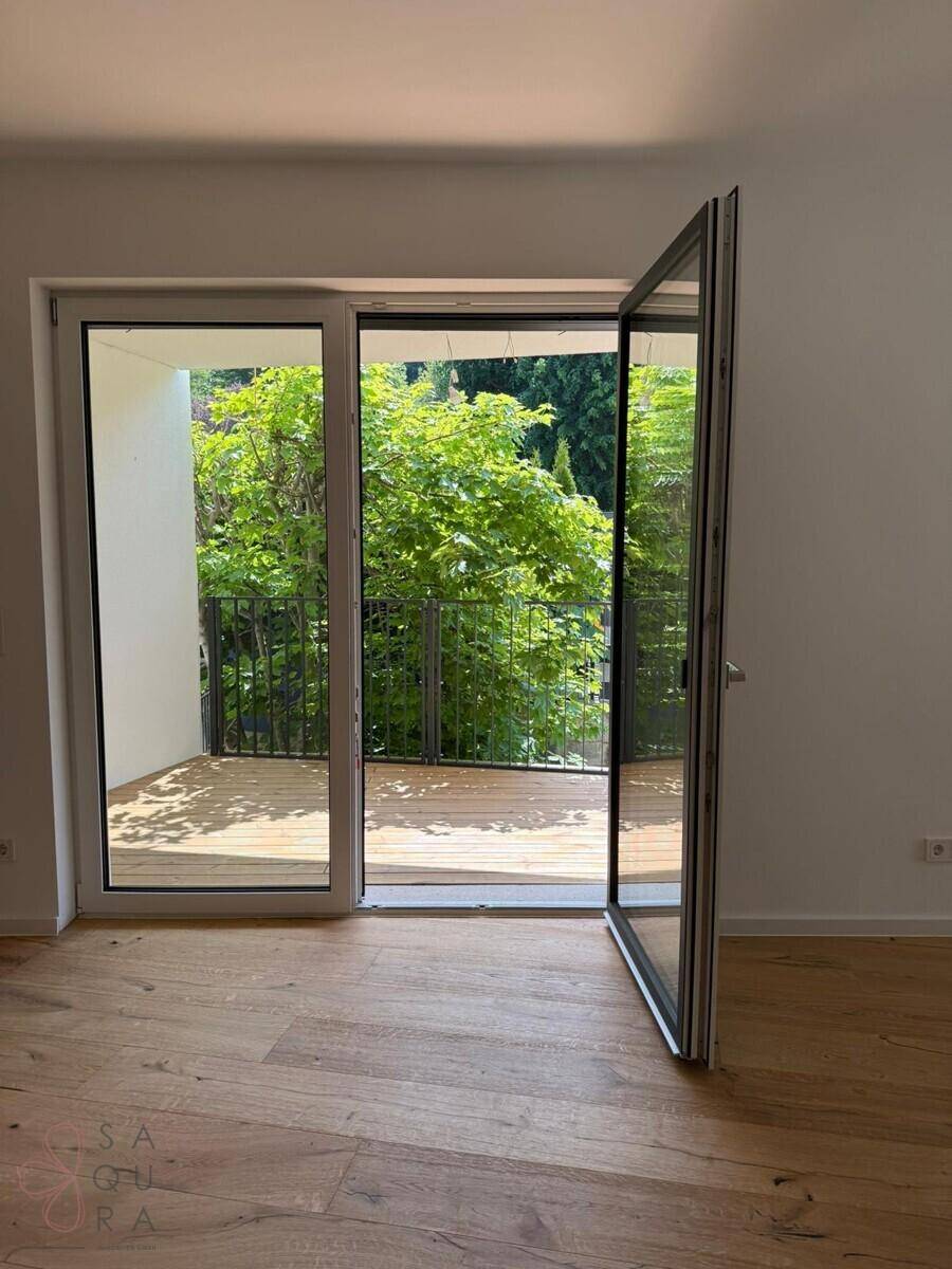 Heller Innenraum mit Holzboden und großen Fenstern, die Zugang zu einem Balkon bieten.