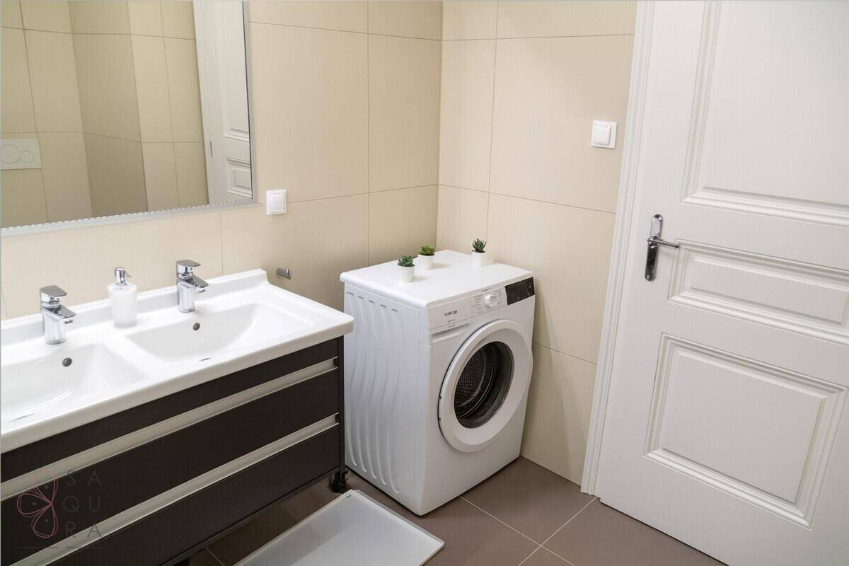 Badezimmer mit Doppelwaschbecken, Spiegelschrank und Waschmaschine, helle Fliesen.