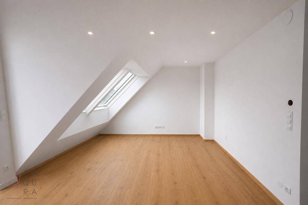 Heller Raum mit Holzboden, Dachschräge und einem Dachfenster für natürliches Licht.