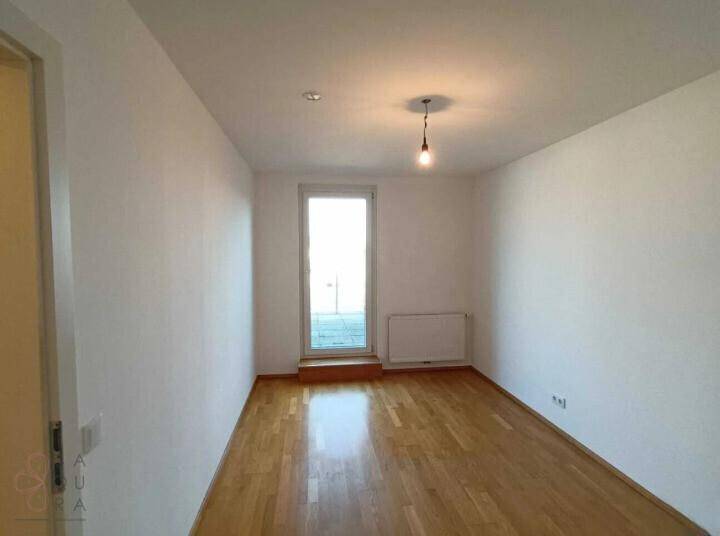 Leeres Zimmer mit hellem Parkettboden und einer Tür, die zu einem Außenbereich führt.