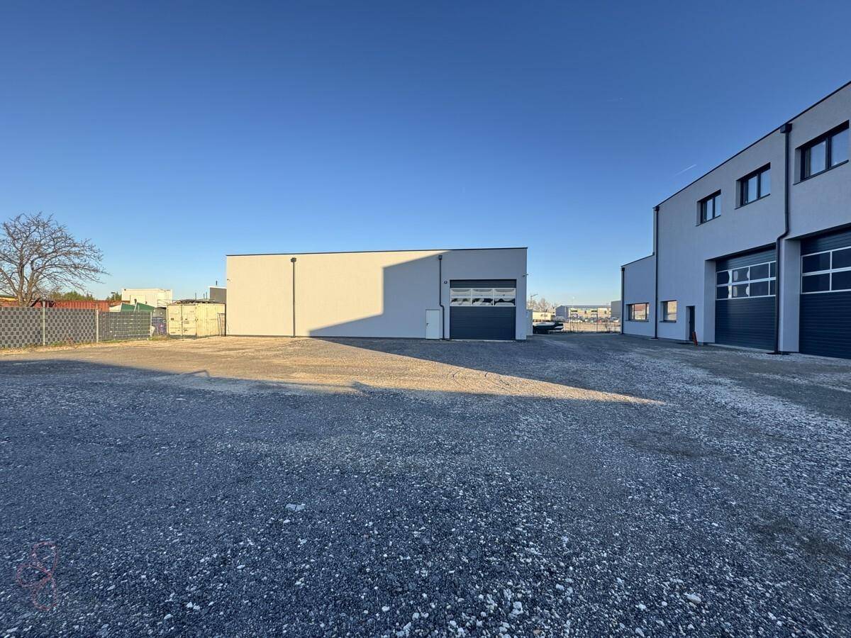 Weitläufige Außenansicht mit zwei Industriegebäuden und einem großen Schotterparkplatz.