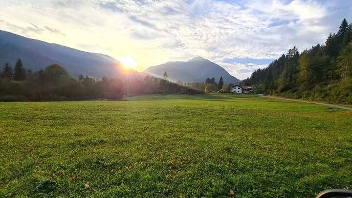 Malerische Landschaft mit weiten grünen Feldern, Bergen im Hintergrund und Sonnenaufgang.