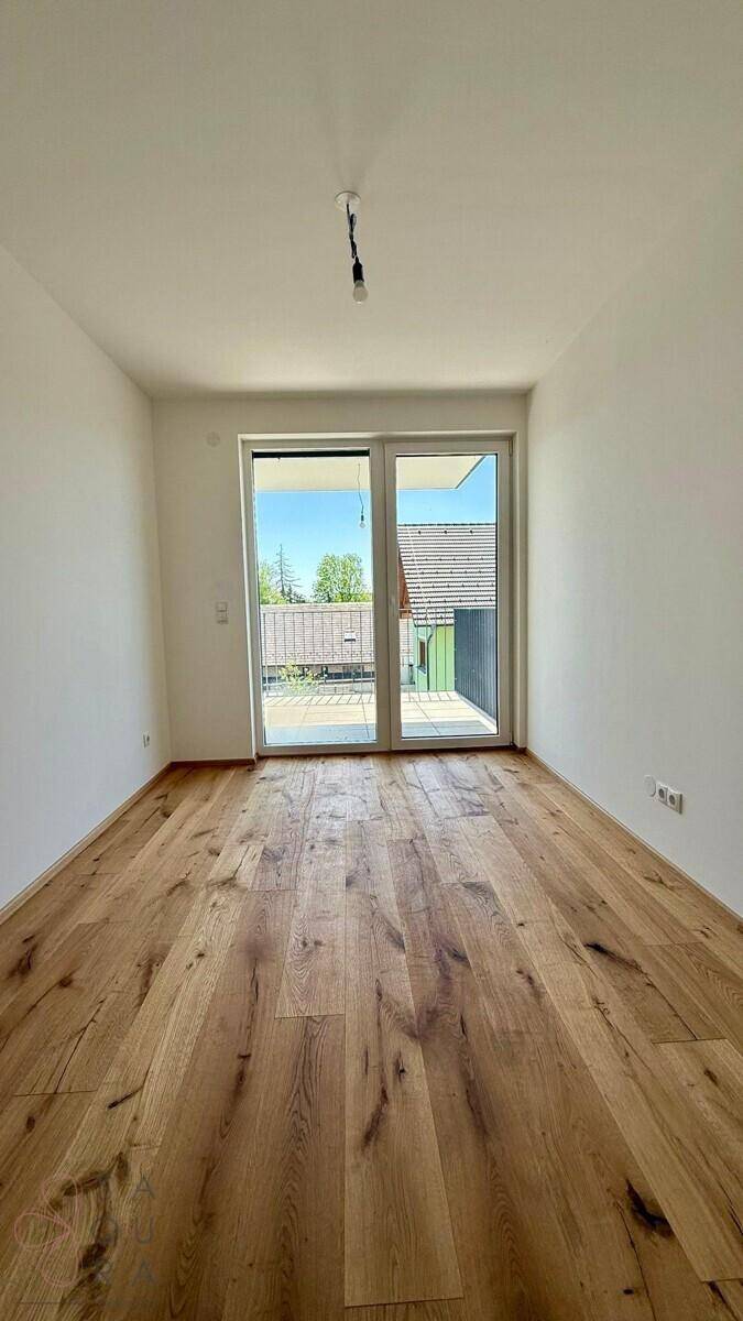 Heller, leerer Raum mit Holzboden und Balkonzugang, bereit für die individuelle Gestaltung.