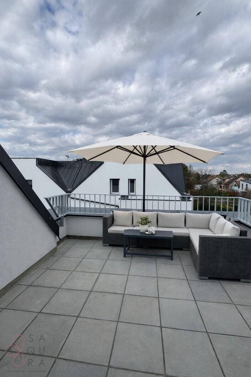 Möblierte Dachterrasse mit Sonnenschirm und bequemen Sitzgelegenheiten unter bewölktem Himmel.