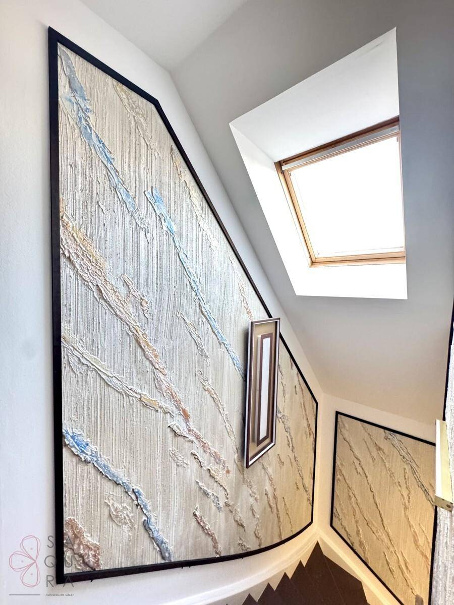 Treppenhaus mit dekorativen Wandpaneelen, Holzgeländer und Dachfenster für Helligkeit.