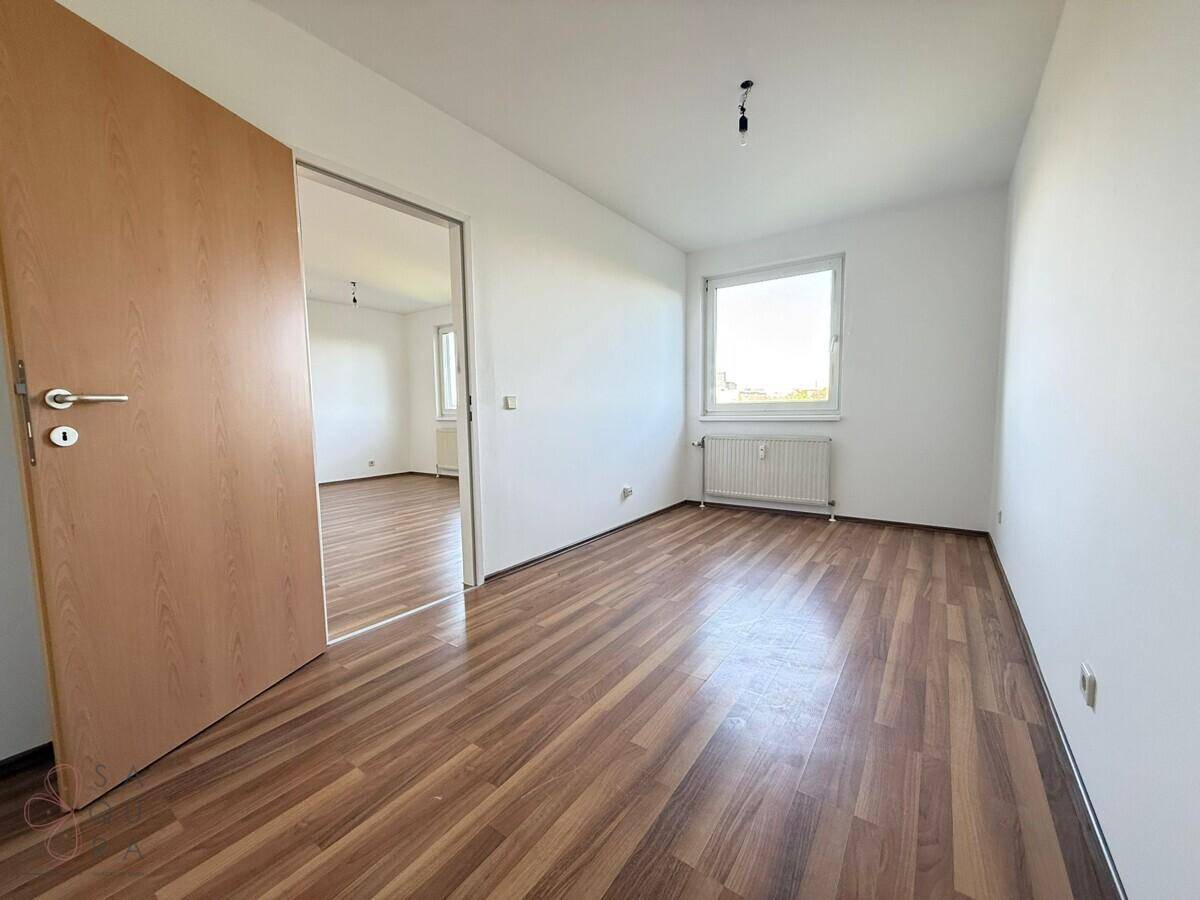 Helles Schlafzimmer mit Laminatboden und Fenster, das zu einem weiteren Raum führt.