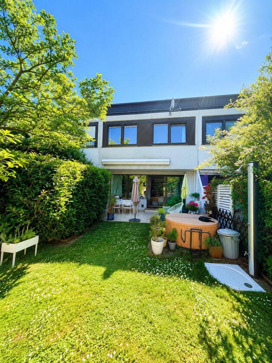 Sonnige Rückseite des Hauses mit gepflegtem Rasen, Terrasse und Whirlpool.