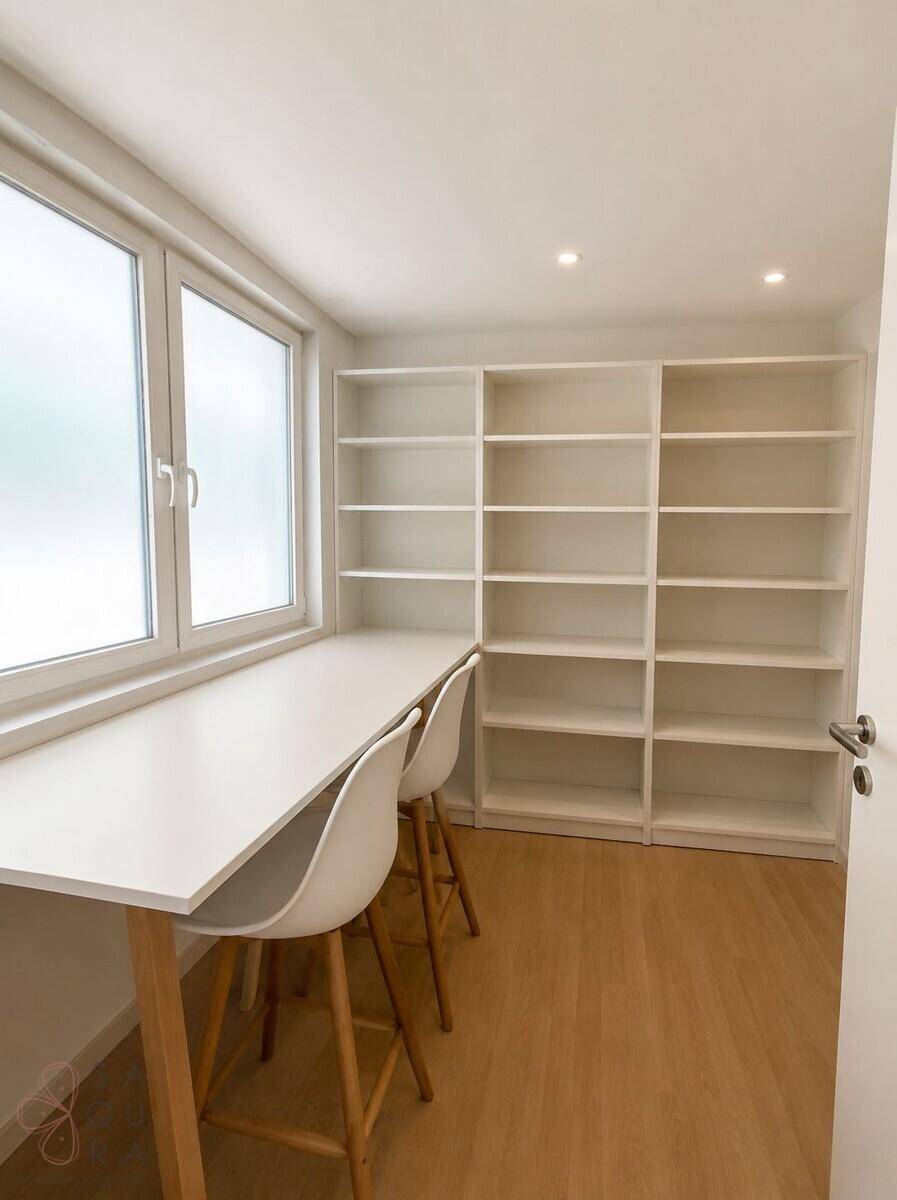 Helles Arbeitszimmer mit großem Fenster, integriertem Schreibtisch und weißen Bücherregalen.