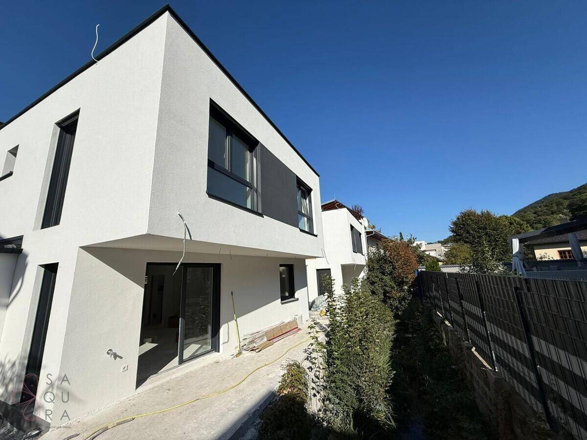 Seitenansicht eines modernen Neubaus mit weißer Fassade und dunklen Fensterrahmen.