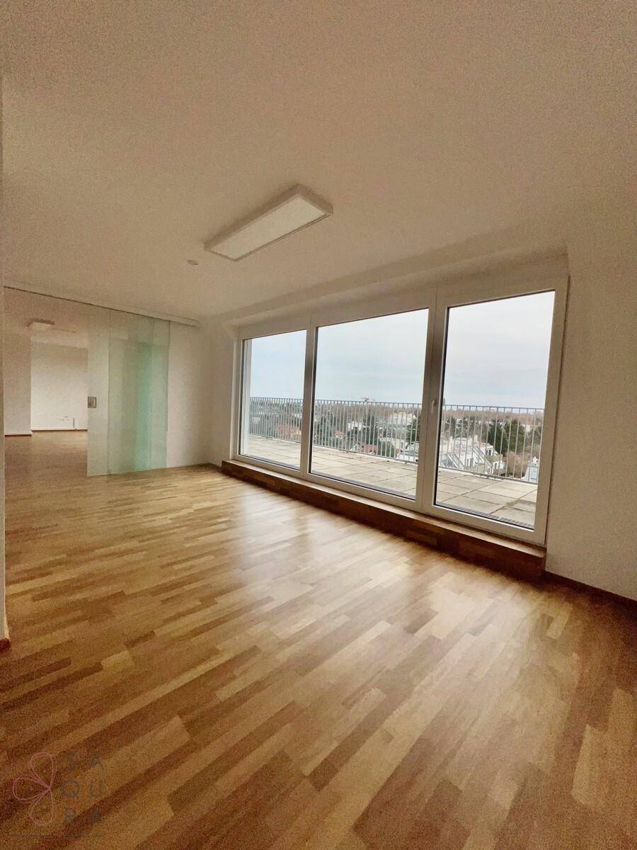 Geräumiger, heller Wohnraum mit Holzboden und großen Fenstern, die einen weiten Blick über die Stadt bieten.