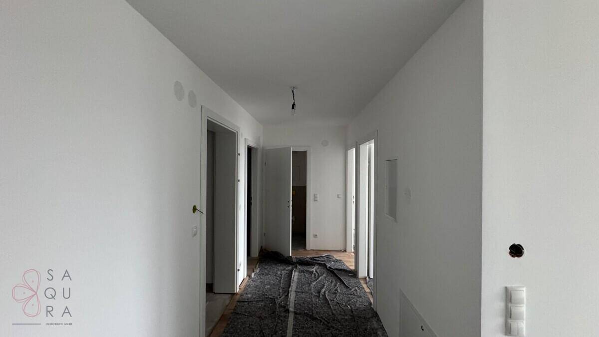 Langer, heller Flur im Bau mit weißen Wänden und mehreren Türöffnungen zu angrenzenden Räumen.