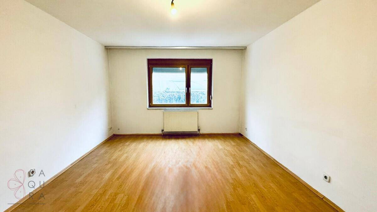 Leeres Schlafzimmer mit Holzboden und Fenster, das einen weiten Blick in die Landschaft bietet.