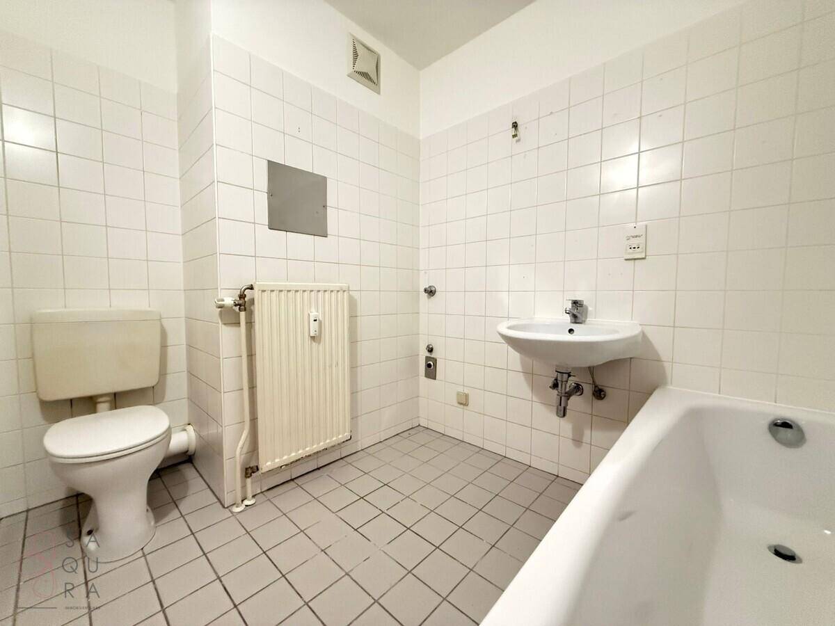 Funktionales Badezimmer mit weißen Fliesen, Badewanne, Toilette und Waschbecken.