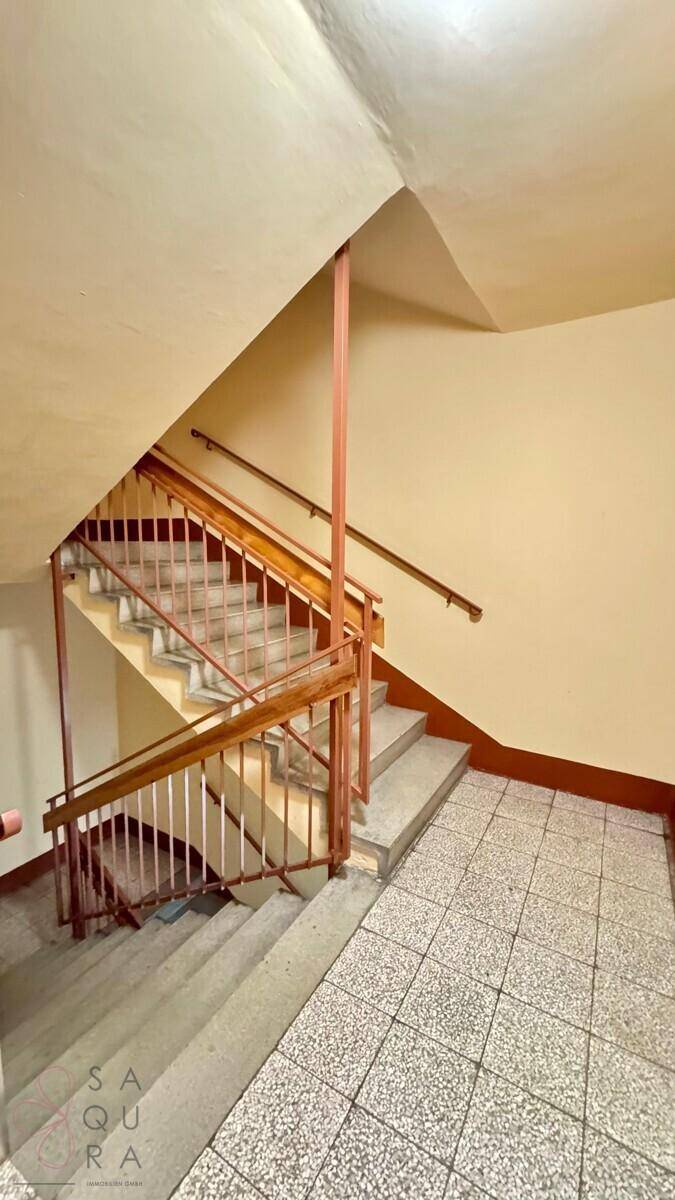 Treppenhaus mit Holzgeländer und Fliesenboden, das die verschiedenen Etagen verbindet.