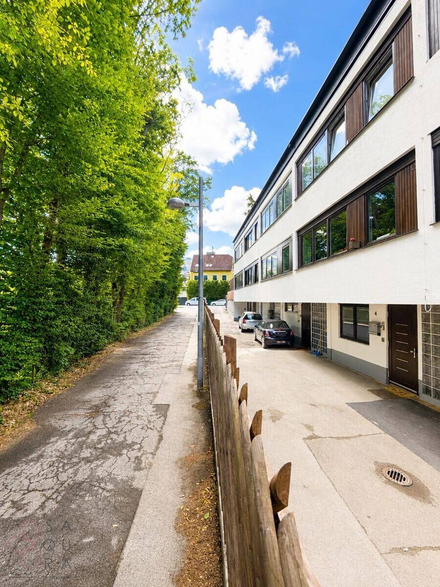Außenansicht des Gebäudes mit Zufahrt, Parkplätzen und umgebender Grünfläche.