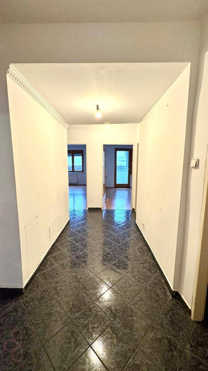 Leerer langer Flur mit dunklem Fliesenboden und Blick in angrenzende, unmöblierte Räume.