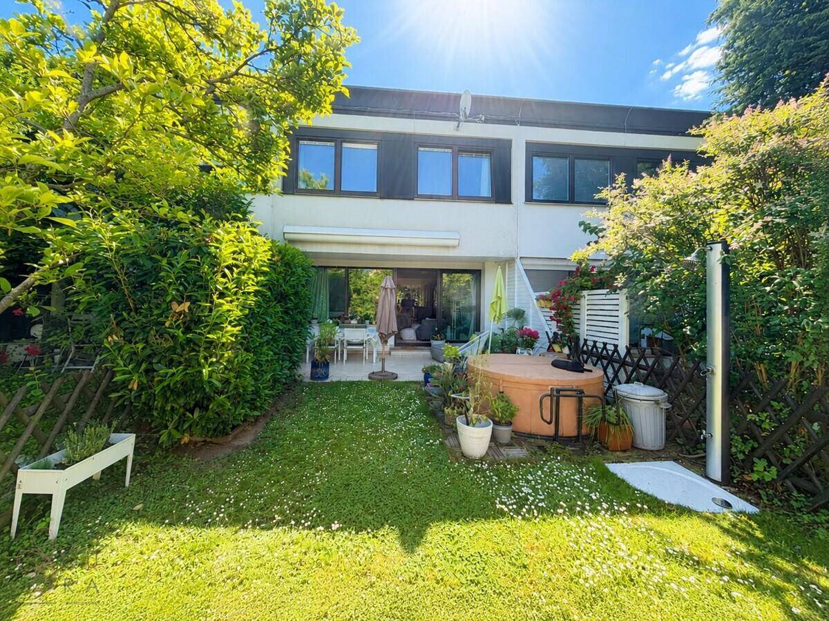 Rückansicht des Hauses mit sonnigem Garten, Terrasse und Whirlpool.