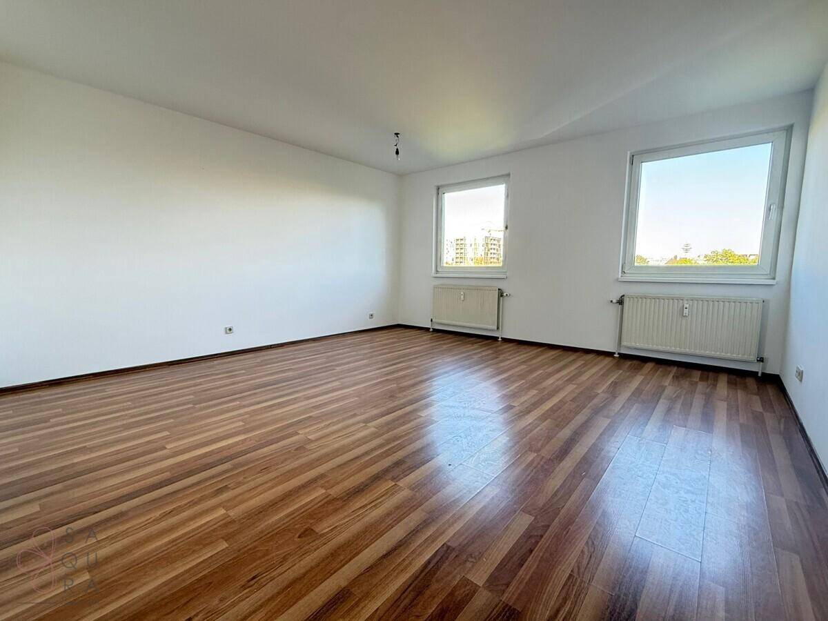 Helles, leeres Wohnzimmer mit Laminatboden und zwei großen Fenstern, bereit zur individuellen Gestaltung.