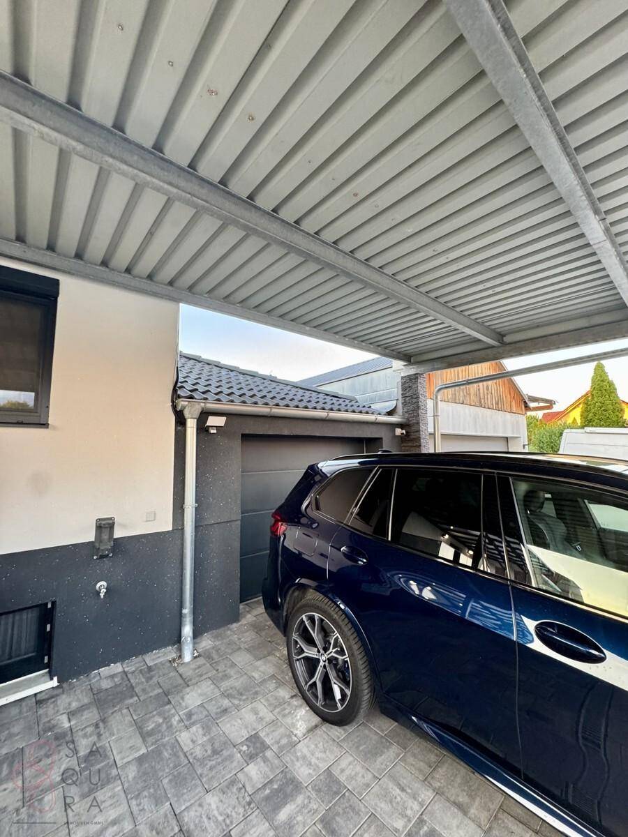 Überdachter Carport-Bereich mit geparktem Auto und Zugang zur Garage des Hauses.