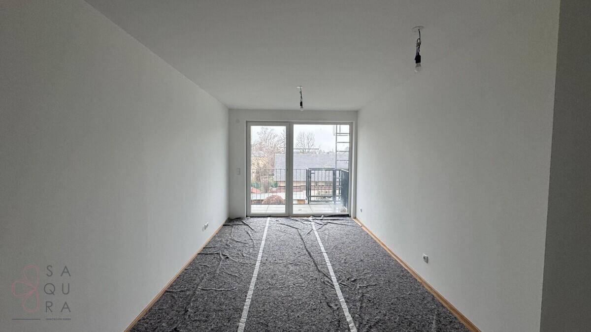 Heller, unmöblierter Raum mit frisch gestrichenen Wänden und Zugang zu einem kleinen Balkon.
