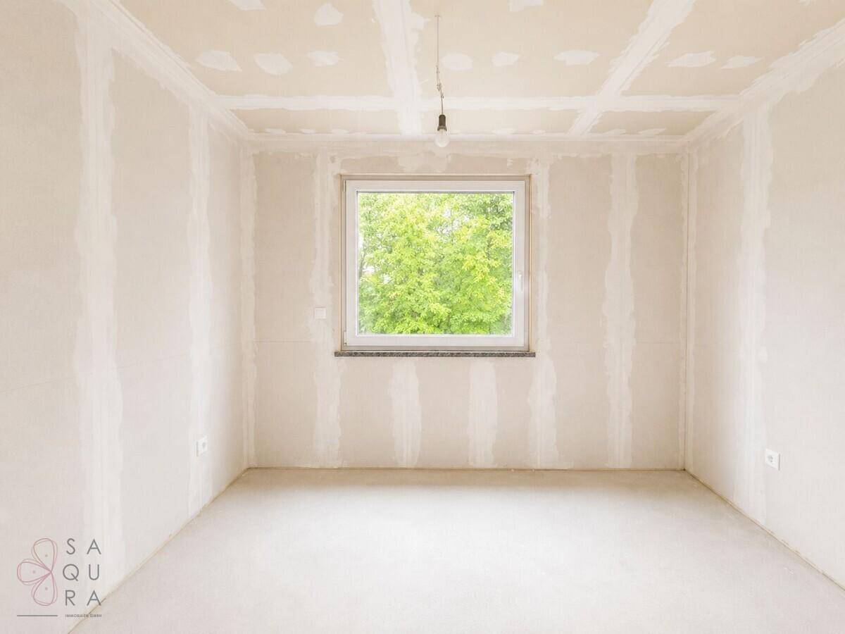 Leerer Raum im Rohbau mit einem Fenster, das viel Tageslicht hereinlässt.