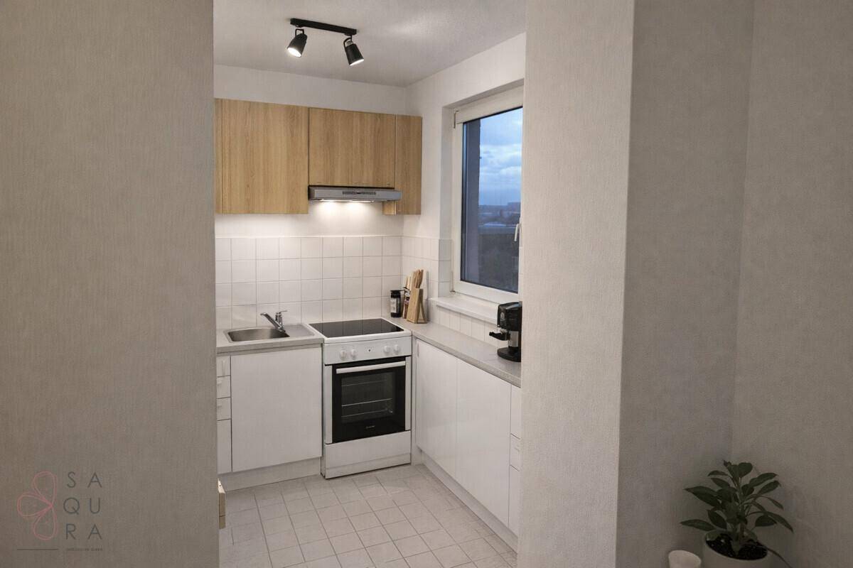 Kompakte, moderne Küchenzeile mit Holzschränken, weißen Fliesen und einem Fenster für Tageslicht.
