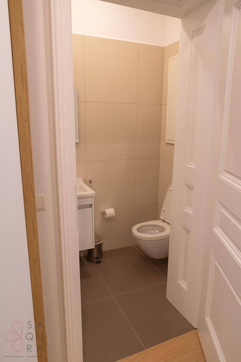 Separates WC mit Waschbecken und Spiegel, helle Fliesen und moderne Ausstattung.