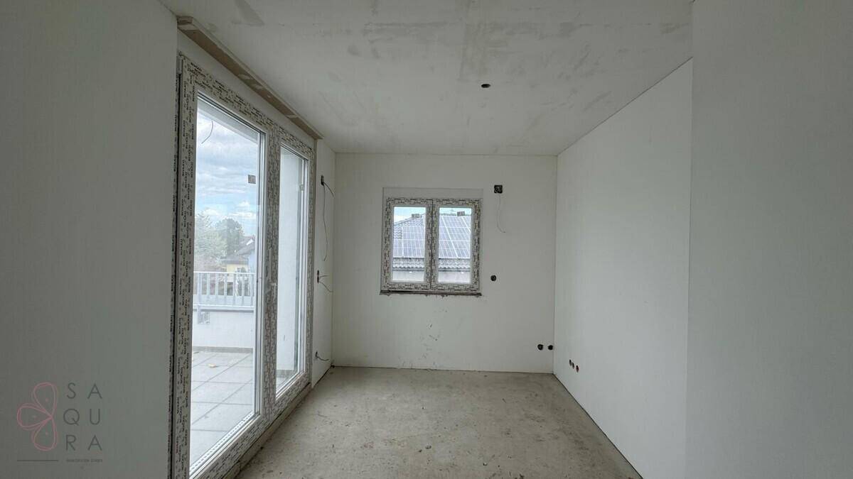 Geräumiges Zimmer im Rohbau mit großem Fenster und Zugang zu einem Außenbereich.