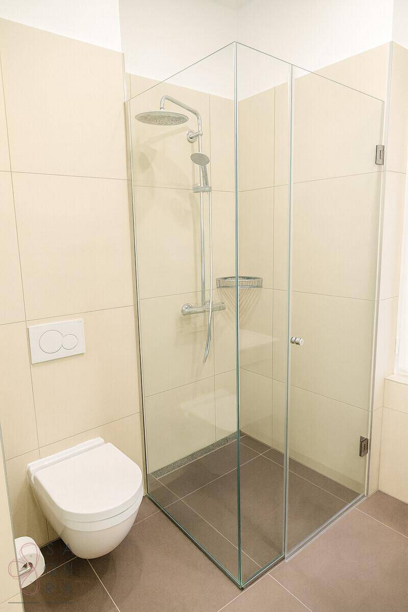 Modernes Badezimmer mit ebenerdiger Glasdusche und wandhängendem WC, helle Fliesen.